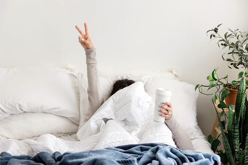 Health Centered Wellness. A woman laying in bed holding a coffee cup.